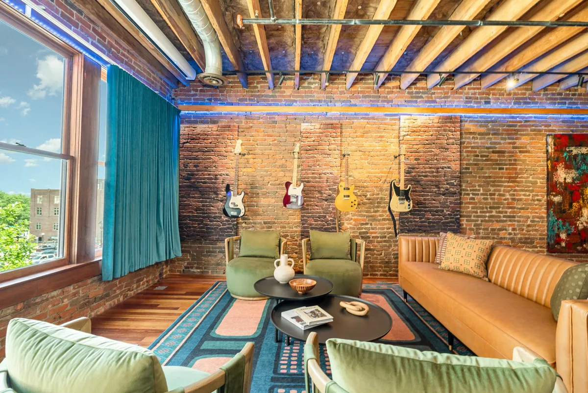 A cozy living space featuring a wall adorned with hanging guitars, a comfortable sofa, a coffee table, and a patterned rug. The setting suggests a relaxed, artistic vibe ideal for conversation or musical collaboration.