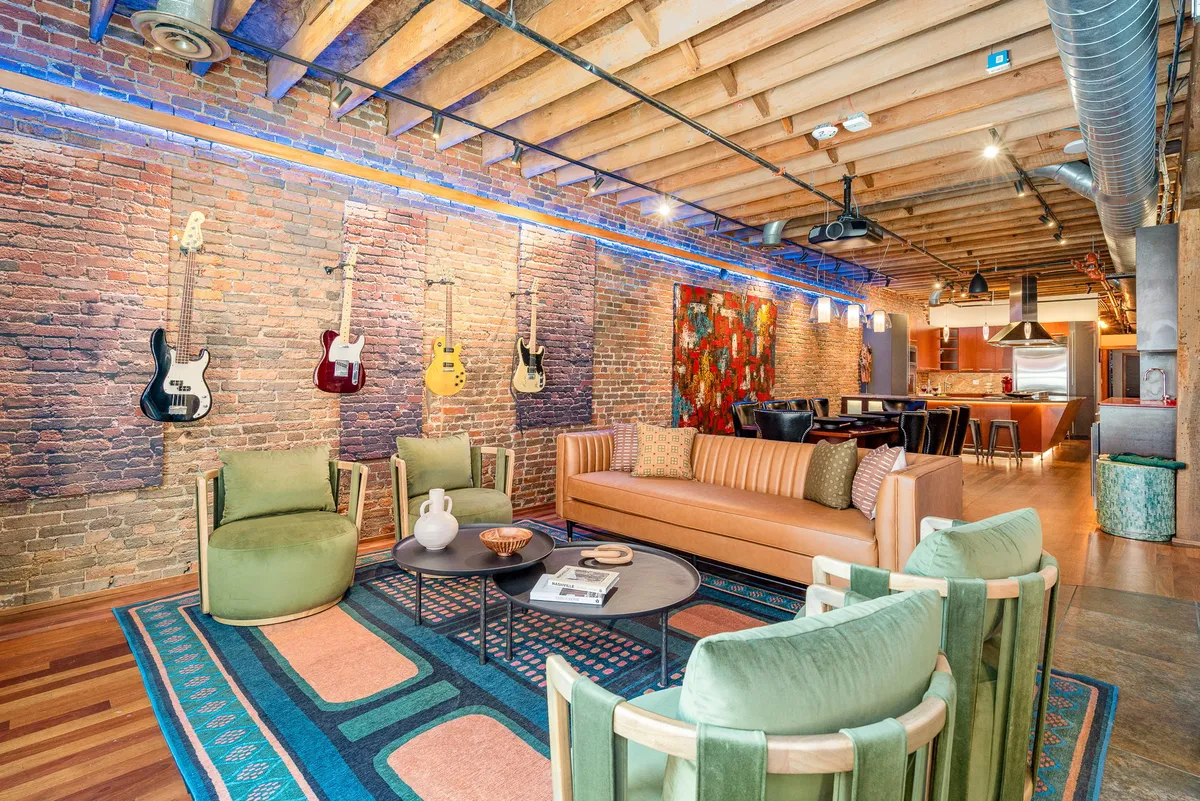 The hero image showcases a stylish, open-concept living space with exposed brick walls, guitars artfully displayed, vibrant artwork, and modern furnishings—evoking the spirit of Nashville's creative scene. The room is set up for socializing, music appreciation, and relaxed gatherings, capturing both the industrial-chic aesthetic and the lively, welcoming atmosphere.
