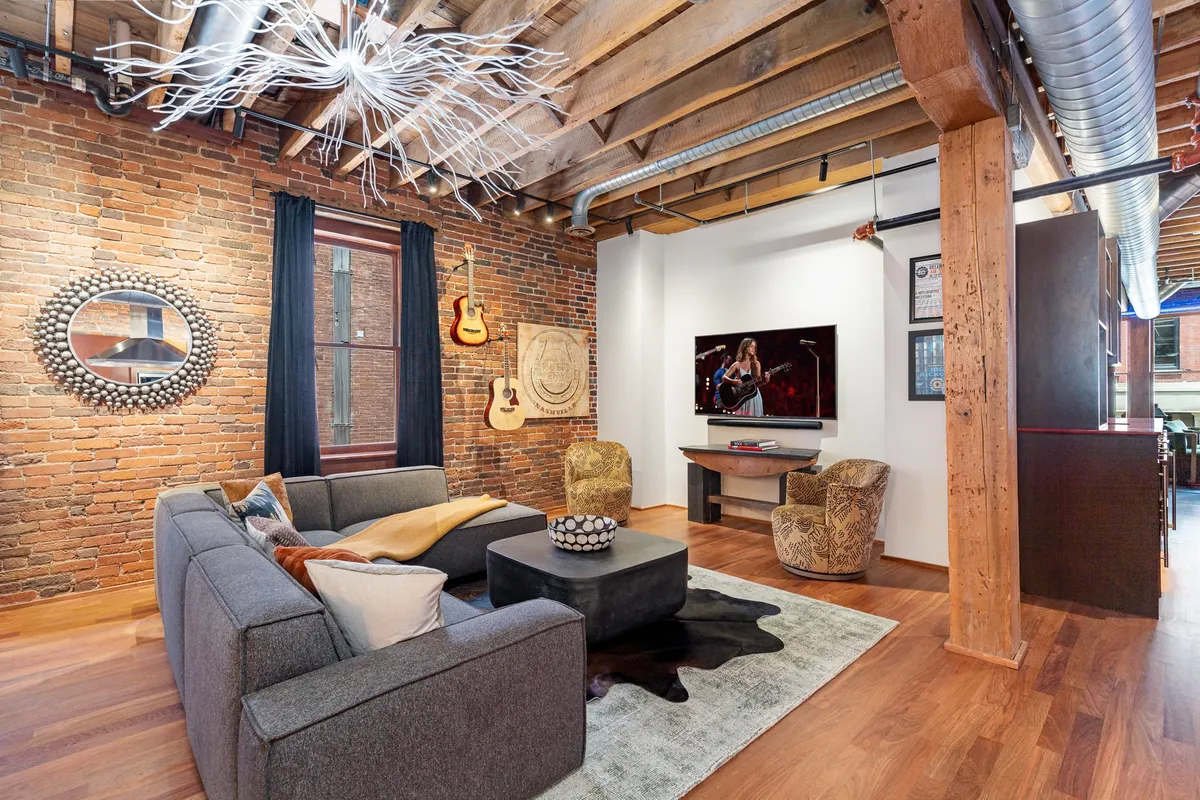 A bright and inviting living area with a sofa, television, eye-catching artwork, and multiple guitars on display. The room feels comfortable and creative, perfect for group movie nights or musical inspiration.