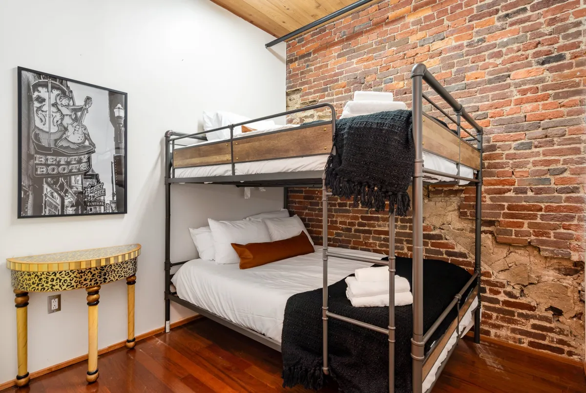 A cozy bedroom featuring queen-over-queen bunk beds, playful artwork, and a unique side table. The design feels welcoming and playful—perfect for group stays, families, or friends sharing late-night conversations.