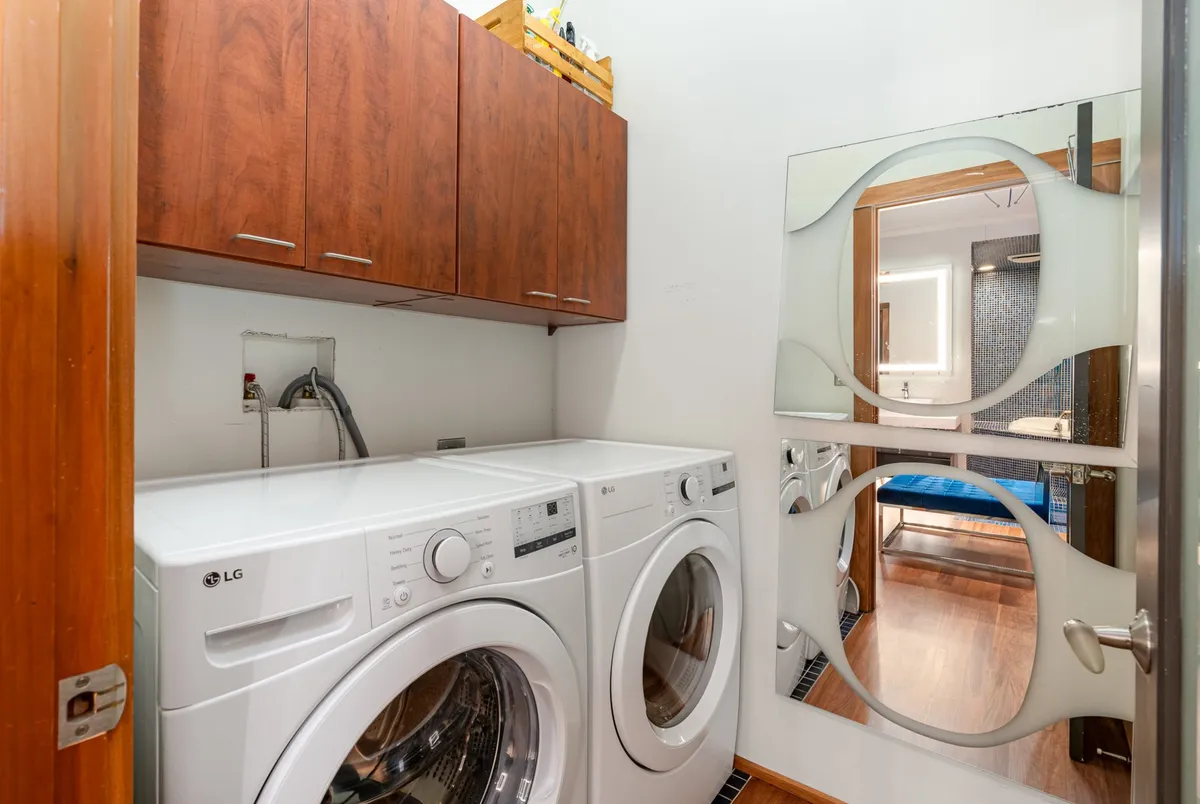 A tidy utility space featuring a washing machine and dryer, wooden cabinets for storage, and a decorative mirror above. The scene is organized and practical, showing off the in-unit laundry capabilities.