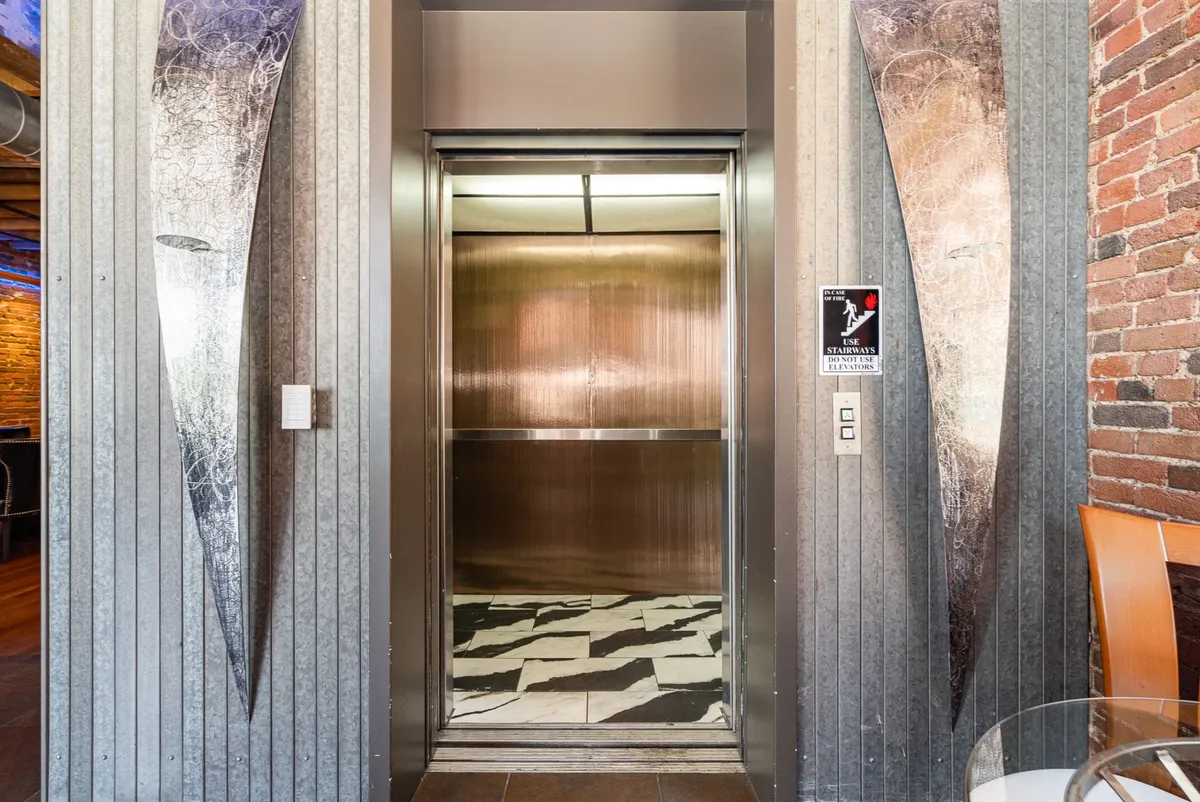 This image shows a modern, well-lit elevator area with artistic wall panels and a marble floor. The elevator doors stand out as a focal point, suggesting both exclusivity and an upscale arrival experience.