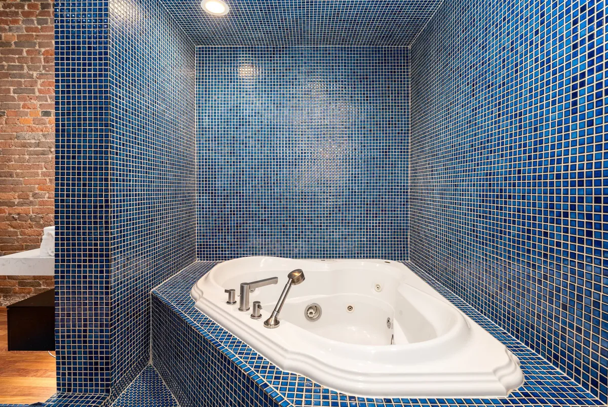 The image captures a tranquil spa bathroom with a luxurious whirlpool tub surrounded by blue mosaic tiles and a backdrop of textured brick walls. The space feels serene and indulgent, ideal for soothing soaks and self-care routines.