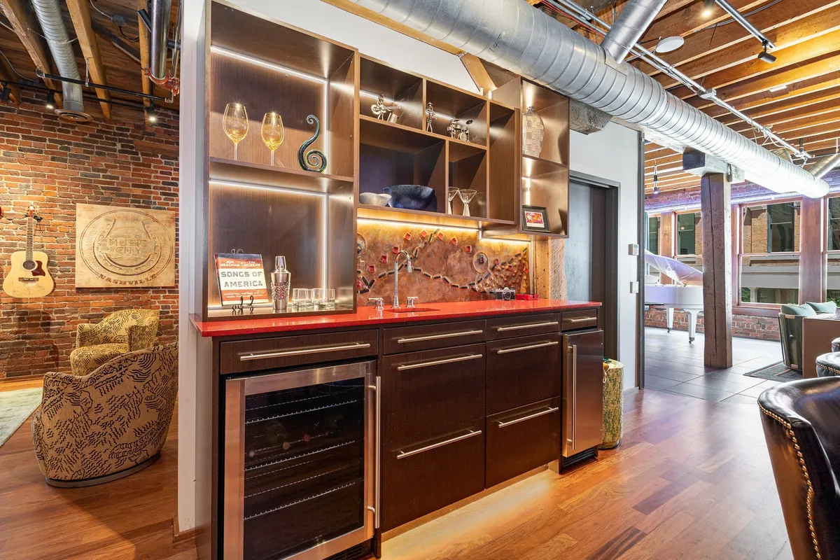 A stylish bar area with a striking red countertop, elegant shelving filled with glassware, and a backdrop of exposed brick. This intimate space is designed for mixing drinks and socializing.